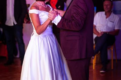 Un couple danse ensemble dans une salle décorée de ballons, entouré de quelques invités en arrière-plan.