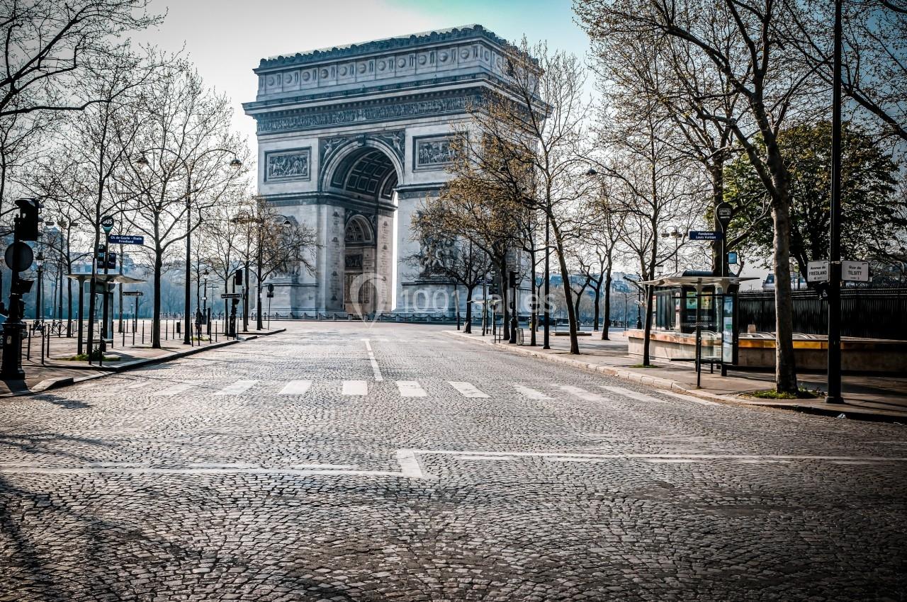 Vue de l'Arc de Triomphe à Paris, entouré d'arbres et de rues pavées, par une journée ensoleillée.