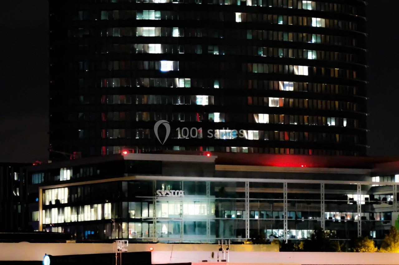 Immeuble moderne éclairé la nuit avec le logo ’Accor’ visible au sommet, entouré de bâtiments et de lumières urbaines.