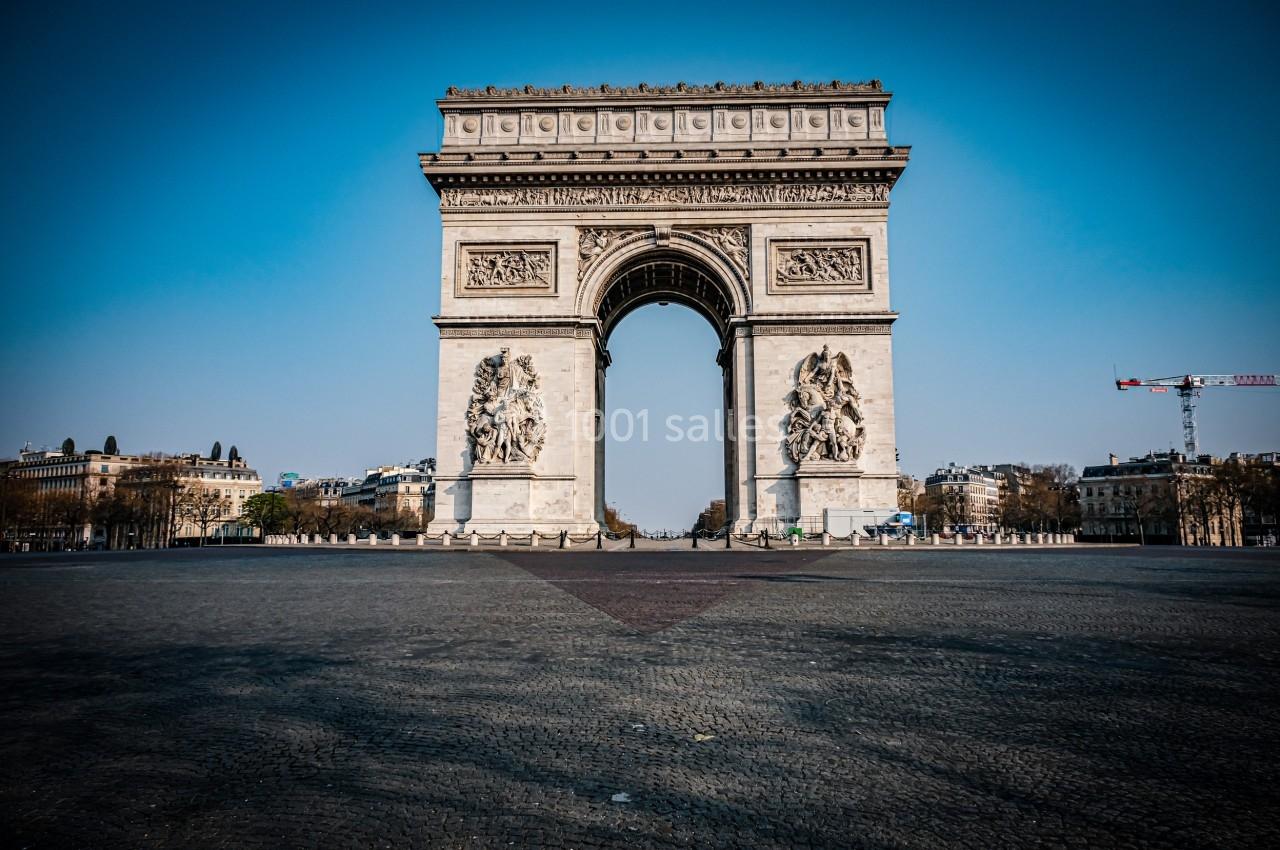 Vue frontale de l'Arc de Triomphe à Paris, entouré d'une place pavée et d'un ciel dégagé.