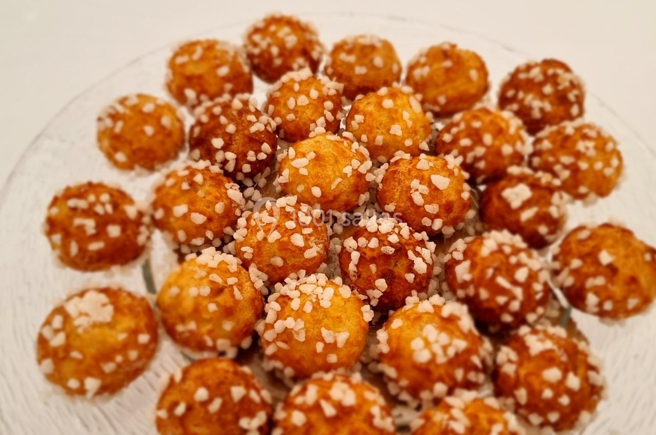 Assortiment de chouquettes dorées garnies de sucre perlé, disposées sur une assiette transparente.