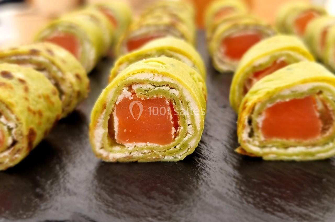 Roulés de crêpes vertes garnis de saumon et fromage frais, présentés sur une ardoise noire.