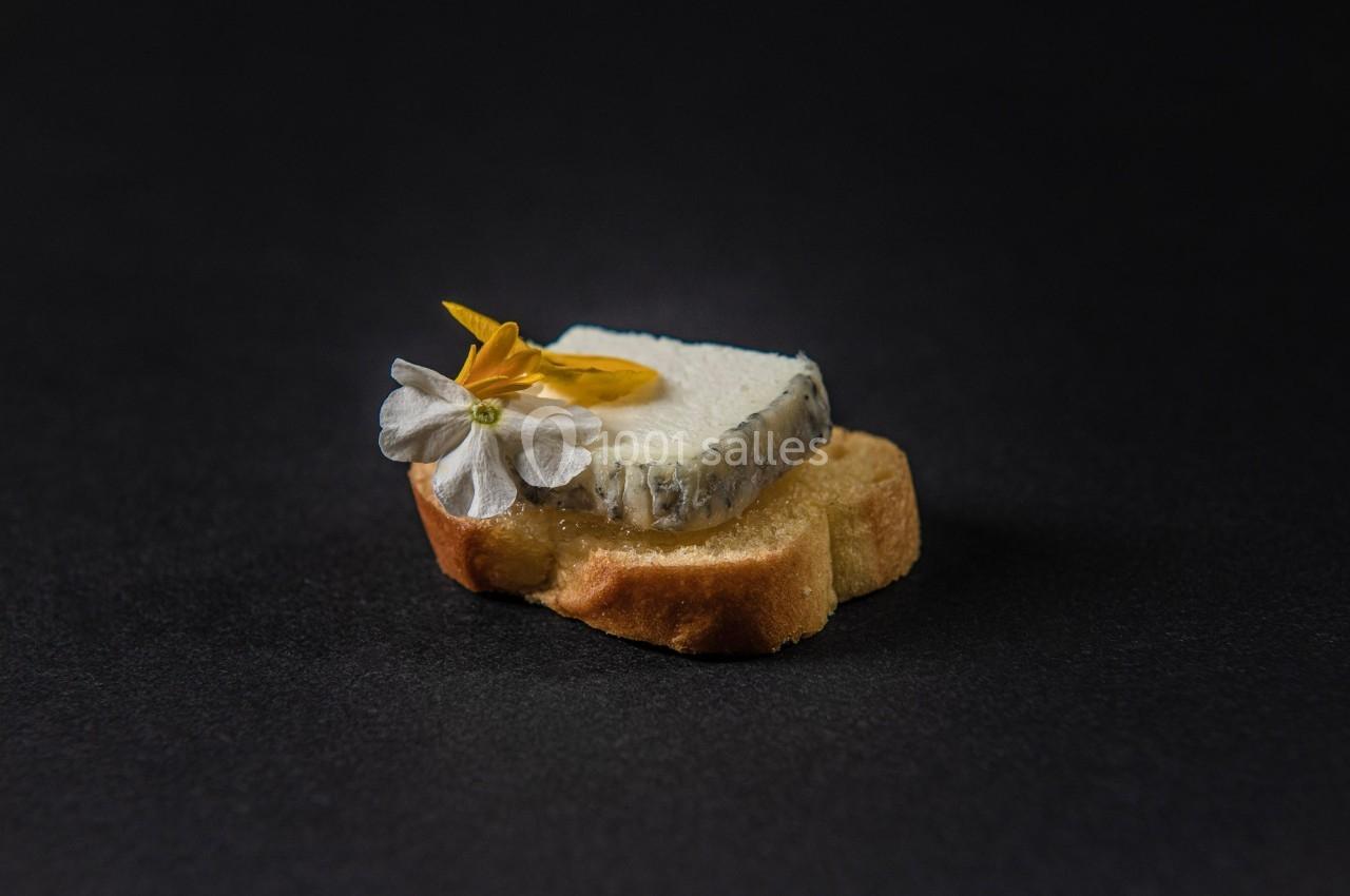 Tranche de fromage sur un toast, décorée de fleurs comestibles, posée sur un fond noir.