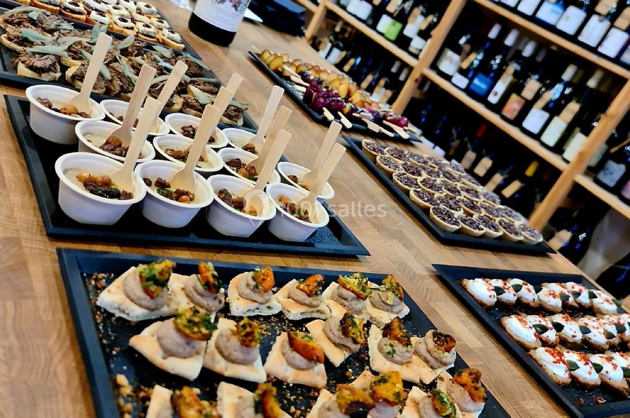 Plateau de tapas variés disposés sur une table en bois, avec des bouteilles de vin en arrière-plan.