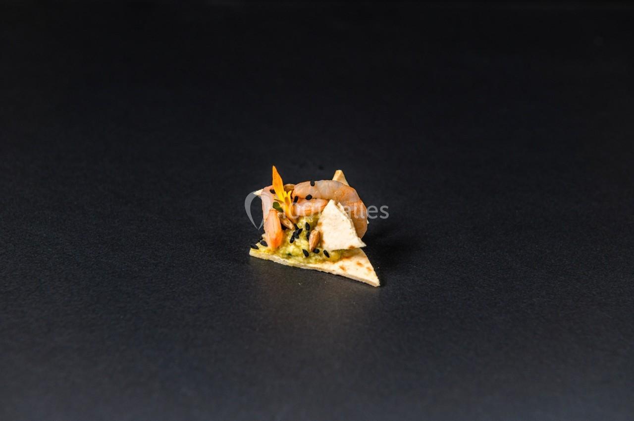 Un petit crabe posé sur un morceau de tortilla garni de guacamole, sur un fond noir.