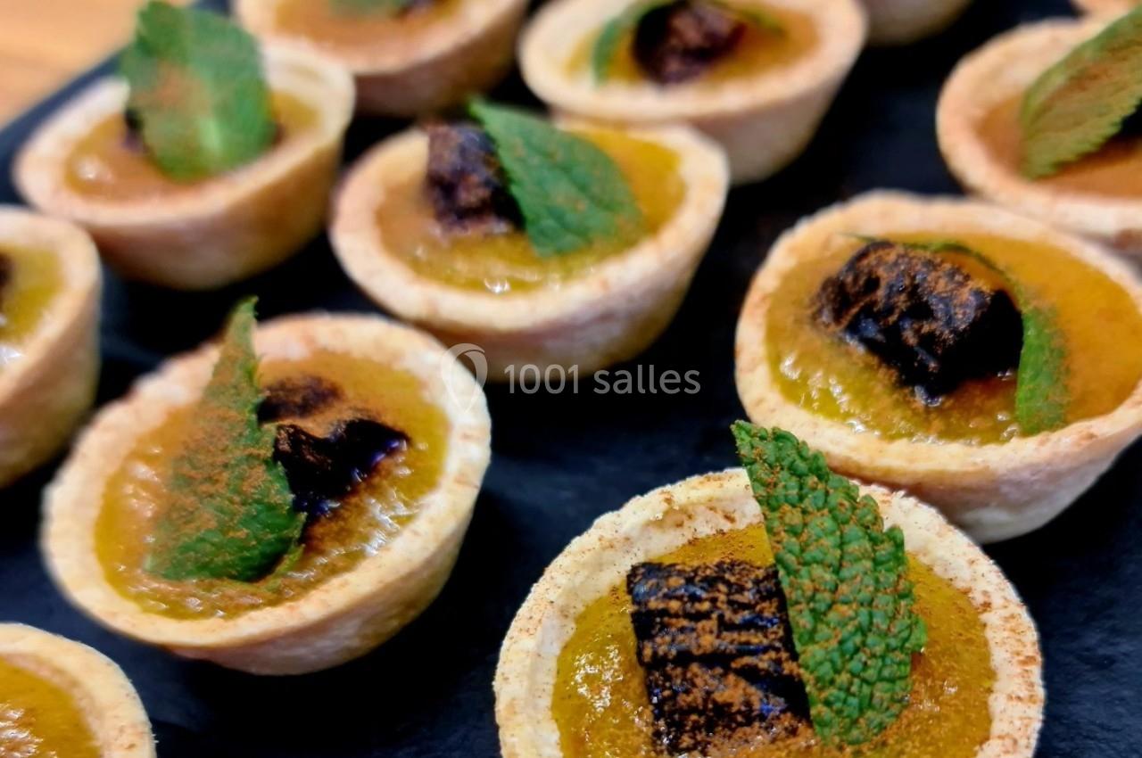 Petites tartelettes garnies de crème orange, décorées de feuilles de menthe et morceaux de chocolat, sur un plateau noir.