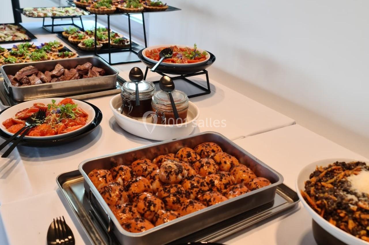 Buffet avec plats variés, incluant salades, pâtes, boulettes et sauces, disposés sur une table blanche.