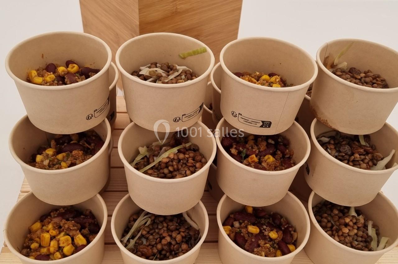 Petits pots en carton remplis de lentilles, maïs et légumes, disposés en pyramide sur une surface en bois.