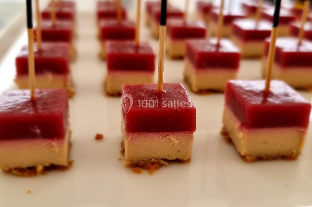 Carrés de foie gras surmontés d'une gelée rouge, présentés avec des pics en bois sur un plateau blanc.