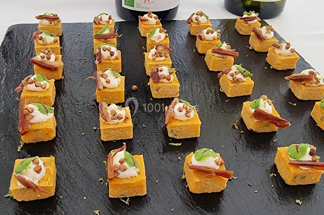 Bouchées apéritives disposées sur une ardoise noire, garnies de crème, anchois et herbes fraîches.