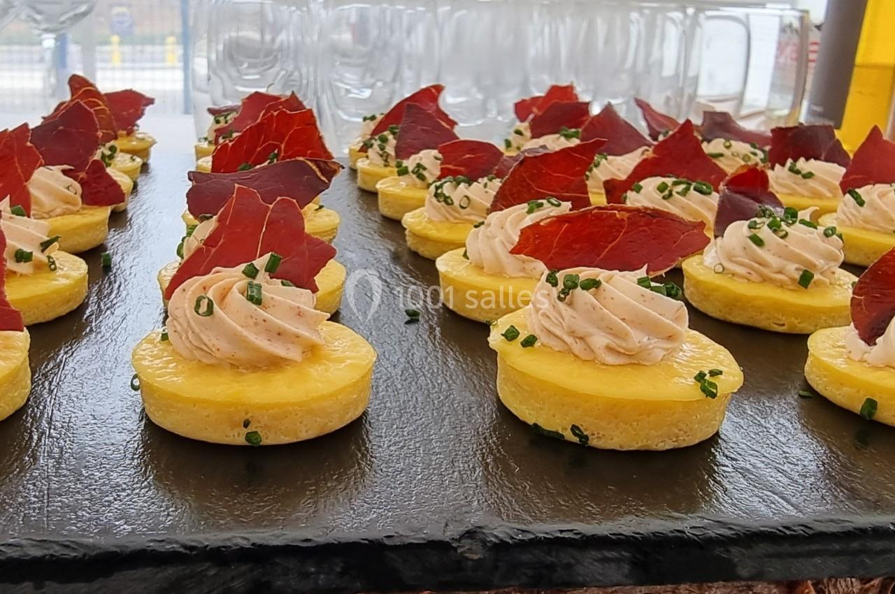 Assortiment de bouchées sur une ardoise, composées de bases dorées, mousse salée, chips rouges et ciboulette.