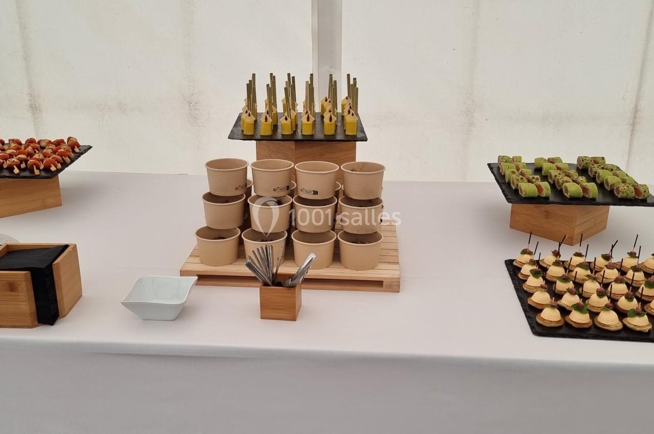 Buffet de bouchées apéritives variées disposées sur une table blanche avec des présentoirs en bois et en ardoise.