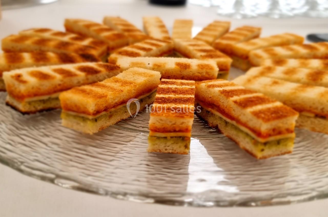 Assortiment de mini-sandwichs grillés disposés en cercle sur une assiette en verre transparente.