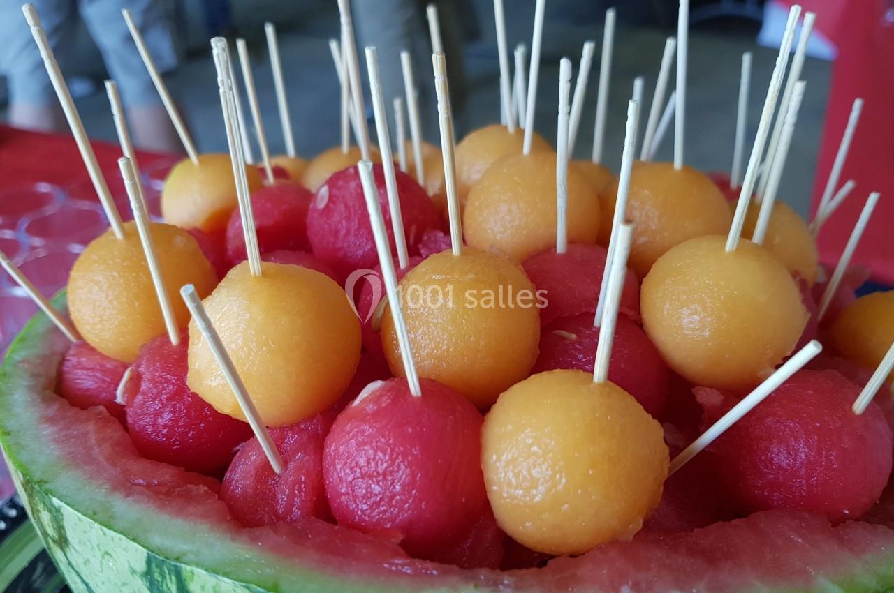 Boules de pastèque et de melon présentées dans une demi-pastèque, avec des piques en bois pour faciliter la dégustation.