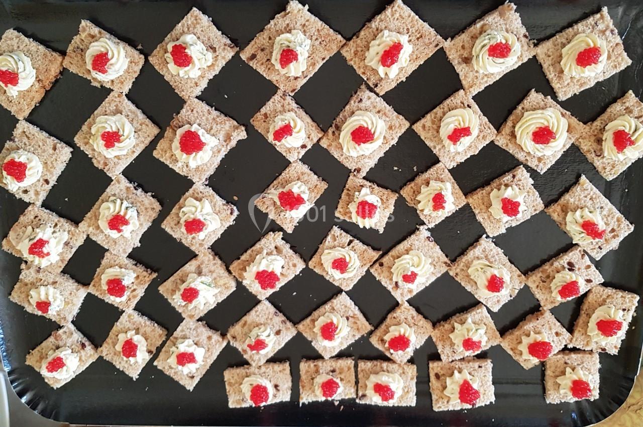 Carrés de biscuits garnis de crème et de petites décorations rouges, disposés en losanges sur un plateau noir.
