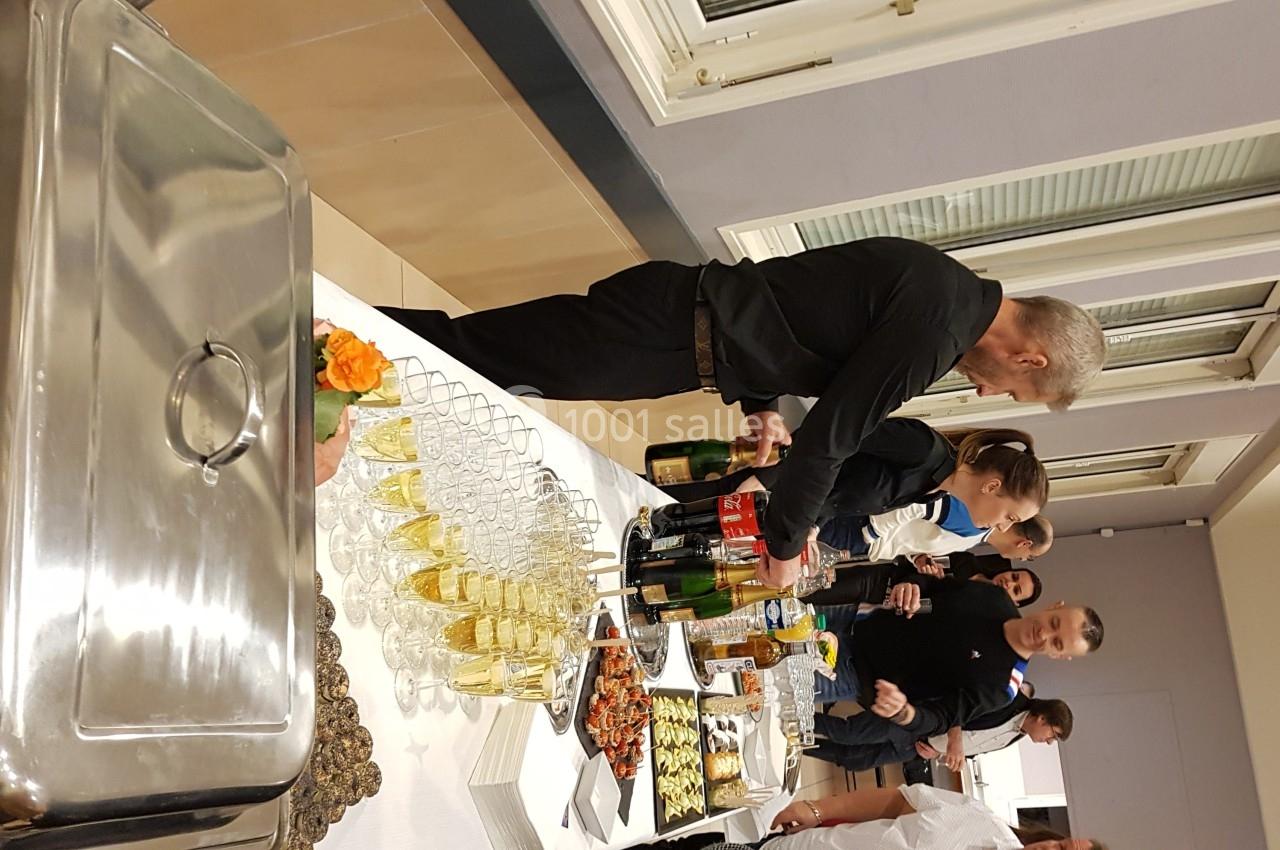 Un buffet avec des boissons, des plats variés et des convives se servant dans une salle lumineuse.