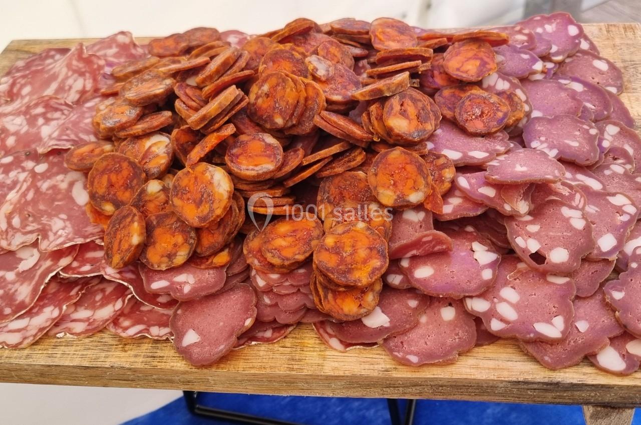 Plateau en bois garni de tranches de charcuterie variée, incluant saucisson, chorizo et saucisse sèche.