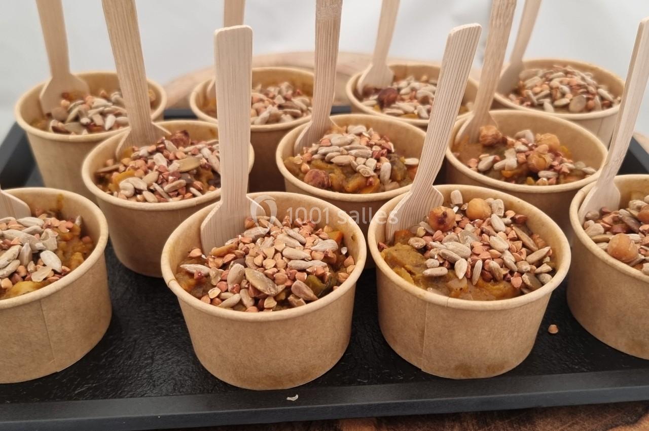 Petits pots en carton remplis de préparation garnie de graines, présentés sur un plateau avec des cuillères en bois.