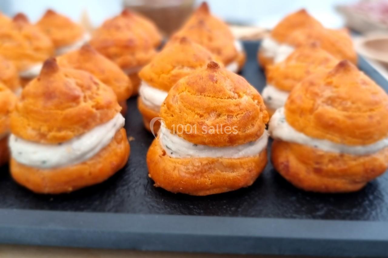 Choux salés garnis de mousse, disposés sur un plateau noir lors d'un buffet ou d'un événement culinaire.