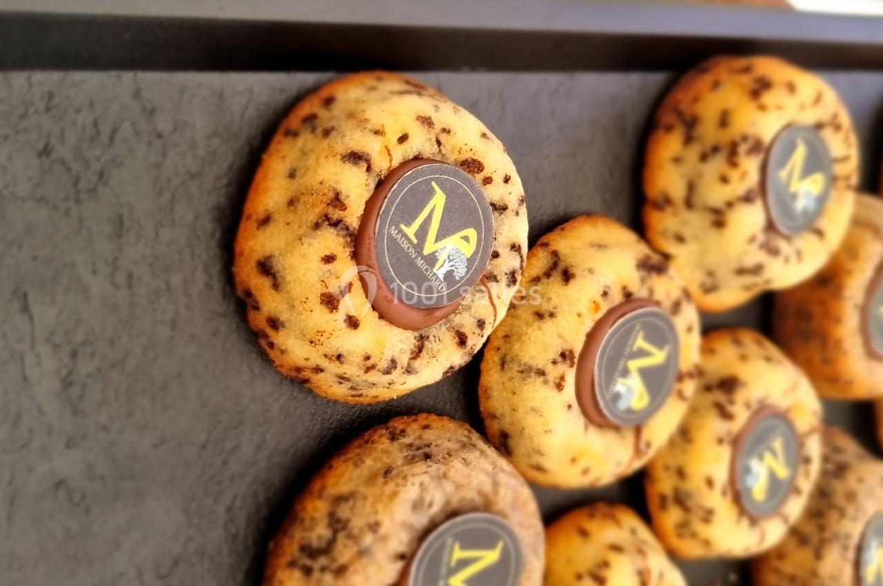 Cookies aux pépites de chocolat disposés sur un plateau noir, chacun décoré d'un disque en chocolat avec un motif doré.