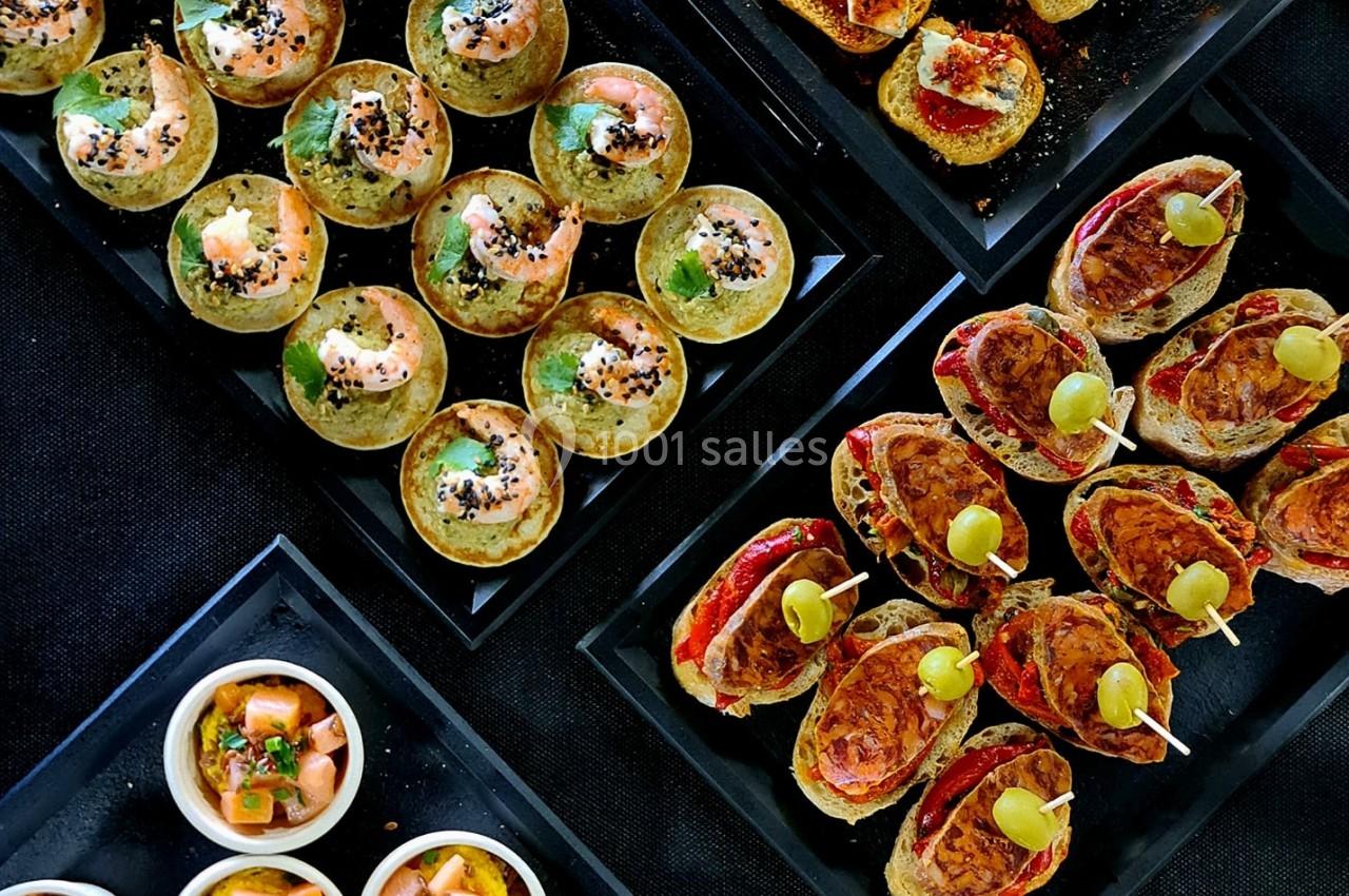 Plateaux de bouchées apéritives variées comprenant canapés, verrines et petits choux sur une table noire.