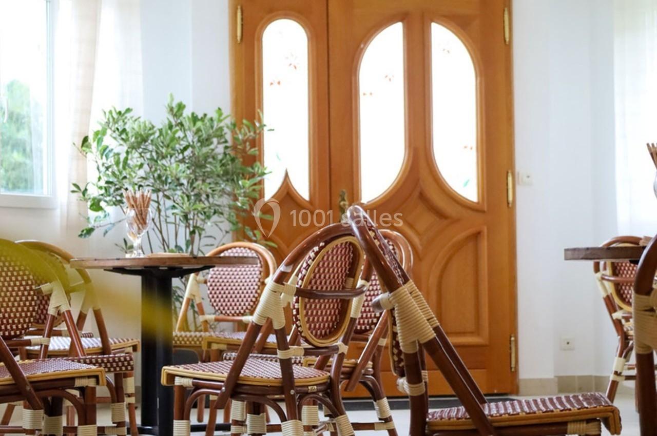 Salle lumineuse avec des chaises en rotin, des tables en bois et une porte en bois sculpté donnant sur l'extérieur.