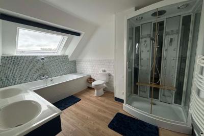 Salle de bain moderne avec douche à paroi vitrée, lavabo rond sur meuble en bois et miroir encadré en rotin.