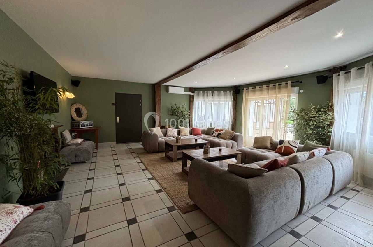 Salon spacieux avec canapés gris, table basse en bois, plantes décoratives et grandes fenêtres laissant entrer la lumière.