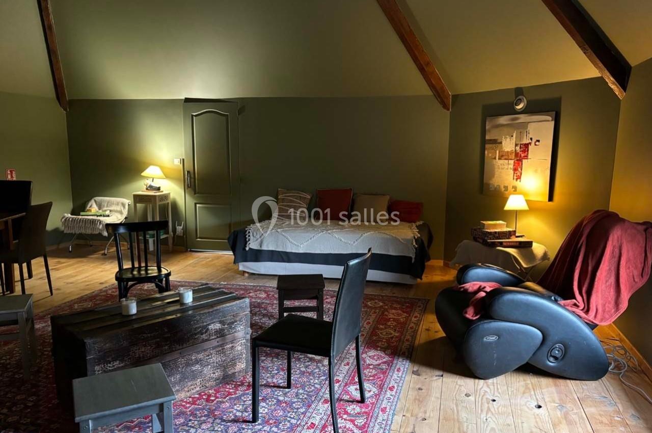 Salon chaleureux avec parquet, tapis coloré, canapé-lit, fauteuil, table basse en bois et éclairage tamisé.