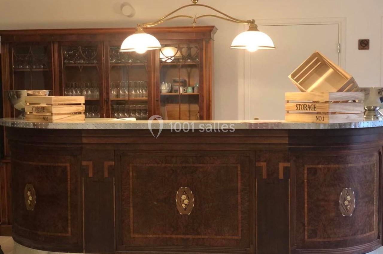 Comptoir en bois sombre avec plateau métallique, éclairé par deux suspensions, entouré de caisses en bois et vaisselier en…