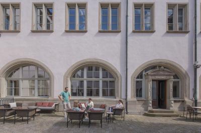 Salle lumineuse avec tables hautes, chaises, grande porte vitrée, fenêtres cintrées et coin kitchenette équipé.