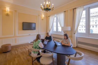 Salle lumineuse avec tables hautes, chaises, grande porte vitrée, fenêtres cintrées et coin kitchenette équipé.