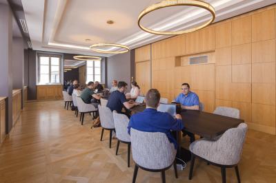 Salle lumineuse avec tables hautes, chaises, grande porte vitrée, fenêtres cintrées et coin kitchenette équipé.