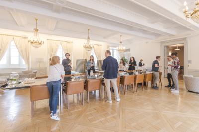 Salle lumineuse avec tables hautes, chaises, grande porte vitrée, fenêtres cintrées et coin kitchenette équipé.