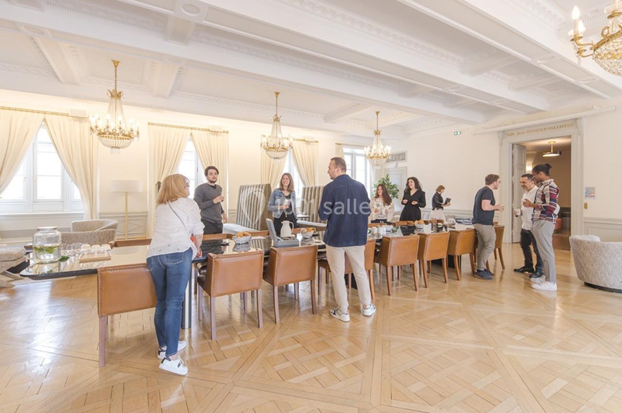 Des personnes discutent autour d'une table dans une salle lumineuse avec parquet, chaises en cuir et lustres.