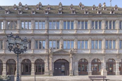 Salle lumineuse avec tables hautes, chaises, grande porte vitrée, fenêtres cintrées et coin kitchenette équipé.