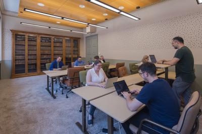 Salle lumineuse avec tables hautes, chaises, grande porte vitrée, fenêtres cintrées et coin kitchenette équipé.