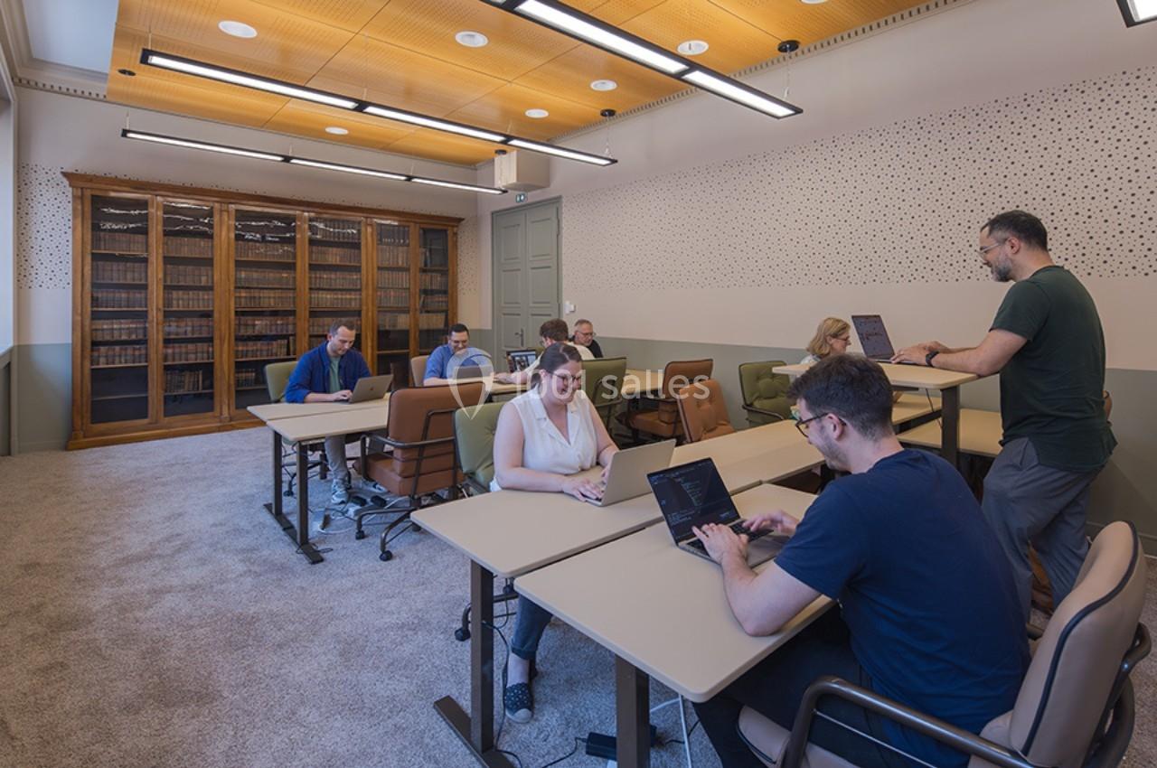 Personnes travaillant sur des ordinateurs portables dans une salle lumineuse avec des étagères de livres en arrière-plan.