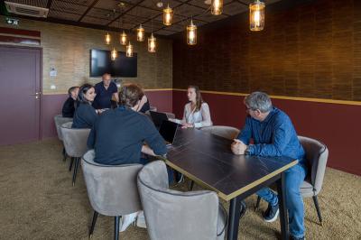 Vue depuis une loge vitrée sur un stade de football vide, avec gradins et pelouse partiellement éclairés.
