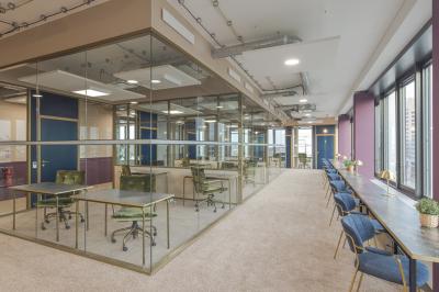 Espace de coworking lumineux avec des plantes, des tables, des chaises et des personnes discutant près d'une kitchenette.