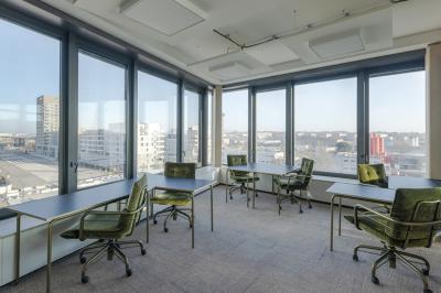 Espace de coworking lumineux avec des plantes, des tables, des chaises et des personnes discutant près d'une kitchenette.
