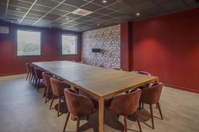 Salle moderne avec tables hautes, chaises rouges, bar en arrière-plan et éclairage suspendu dans un décor industriel.