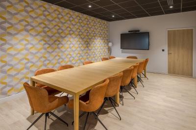 Salle moderne avec tables hautes, chaises rouges, bar en arrière-plan et éclairage suspendu dans un décor industriel.