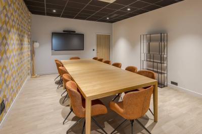 Salle moderne avec tables hautes, chaises rouges, bar en arrière-plan et éclairage suspendu dans un décor industriel.