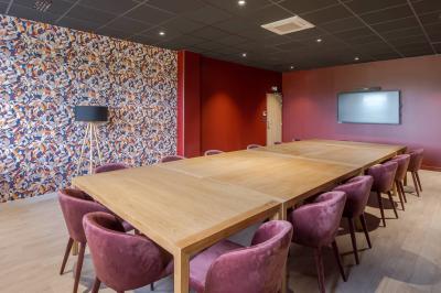 Salle moderne avec tables hautes, chaises rouges, bar en arrière-plan et éclairage suspendu dans un décor industriel.