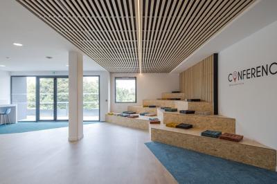 Salle moderne avec tables hautes, chaises rouges, bar en arrière-plan et éclairage suspendu dans un décor industriel.