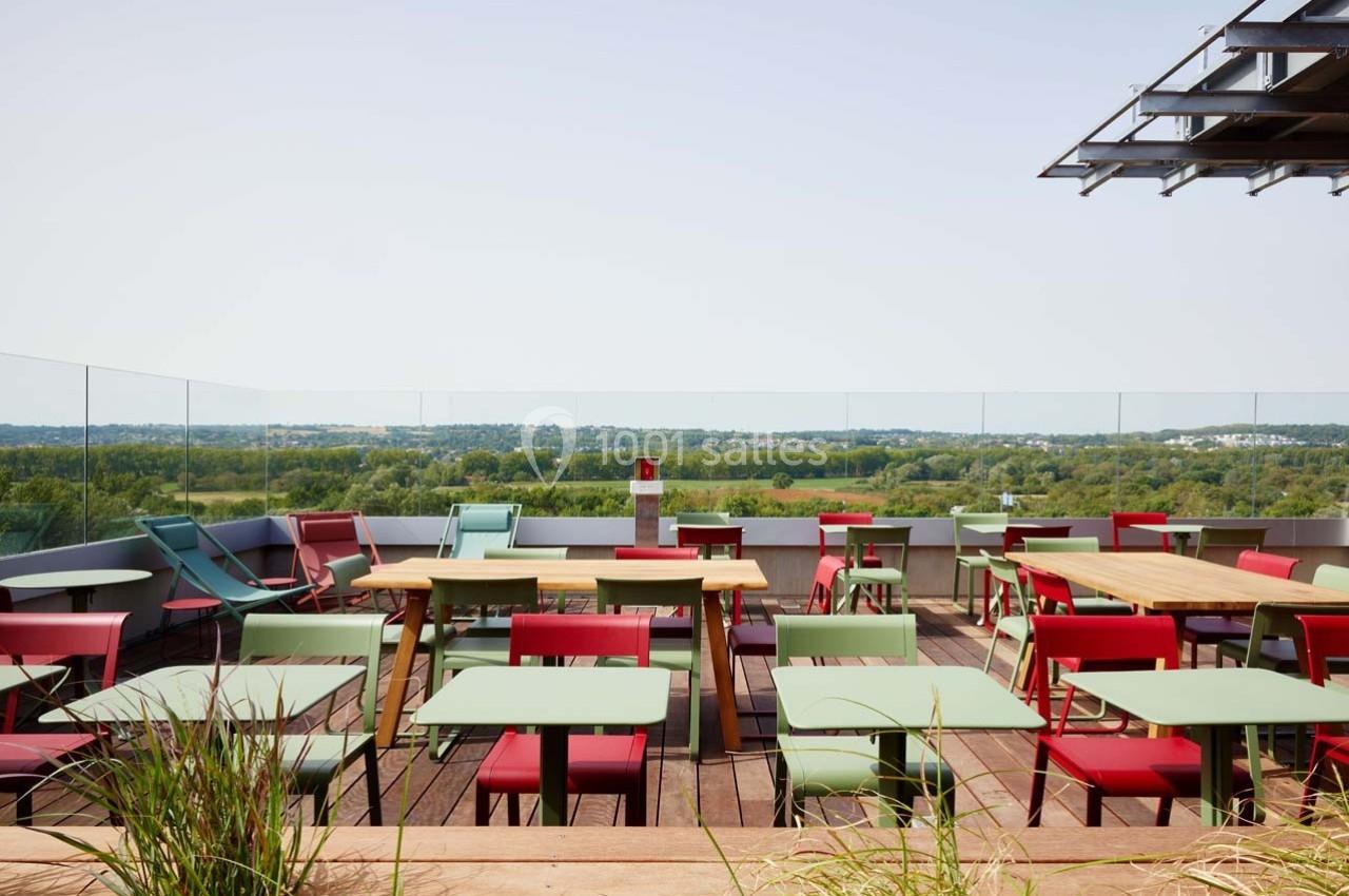 Terrasse avec des tables et chaises colorées, vue dégagée sur un paysage verdoyant à l'arrière-plan.