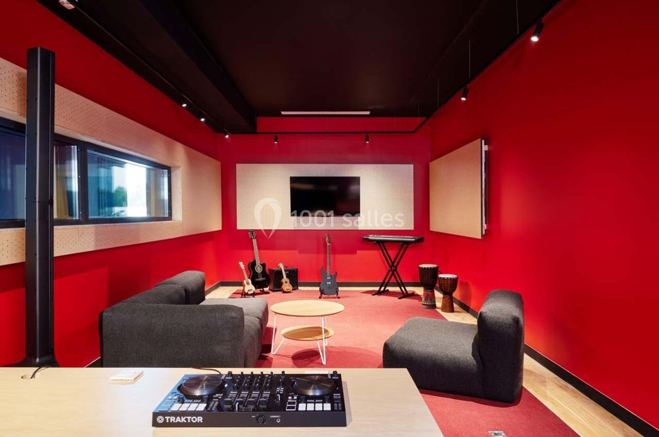 Salle de musique moderne avec murs rouges, instruments variés, canapé, table basse et équipement audio.