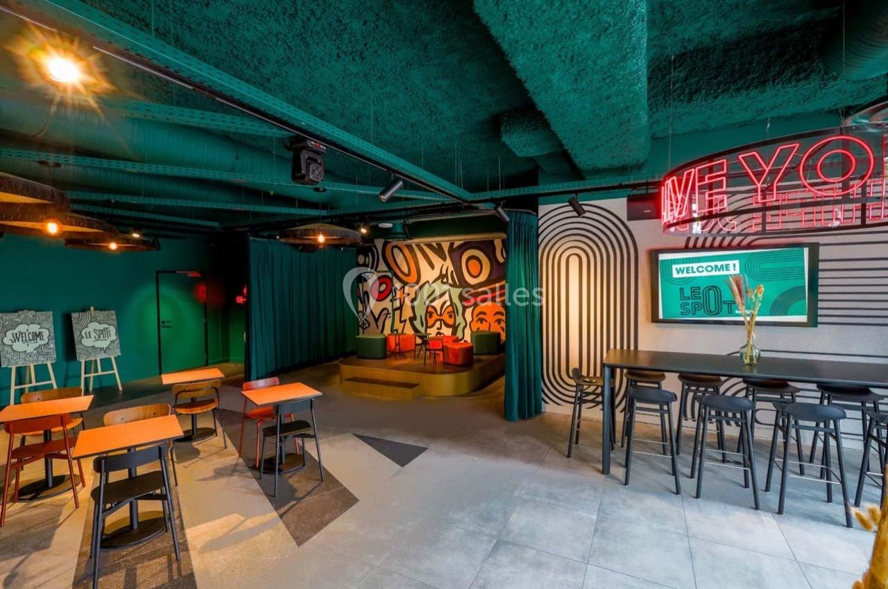 Espace intérieur moderne avec tables, chaises, mur décoré de motifs colorés et enseigne néon.