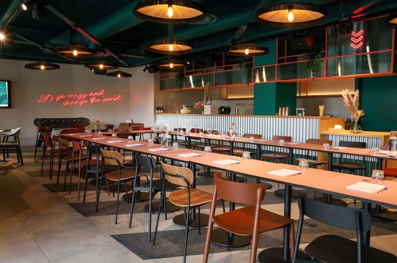 Salle de réunion moderne avec longues tables, chaises variées, éclairage suspendu et décorations murales lumineuses.